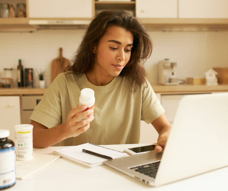 A woman reviewing her medication bottle while on a video call with her laptop