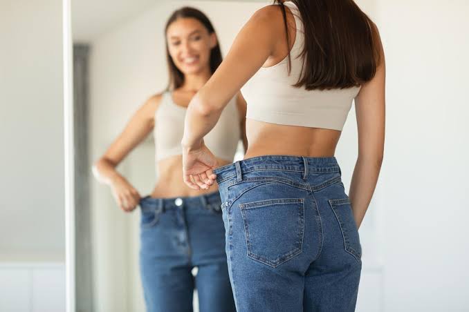 A person admiring their healthy progress in a mirror while wearing comfortable jeans