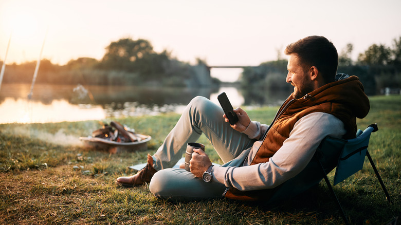 A man relaxing outdoors by a lake at sunset while using his phone for a virtual care visit